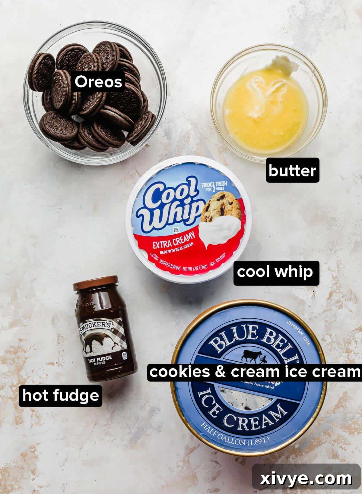 Dreamy Oreo Ice Cream Cake 3 Oreo Ice Cream Cake ingredients in glass bowls: Oreos, butter, oreo ice cream, cool whip, and hot fudge.