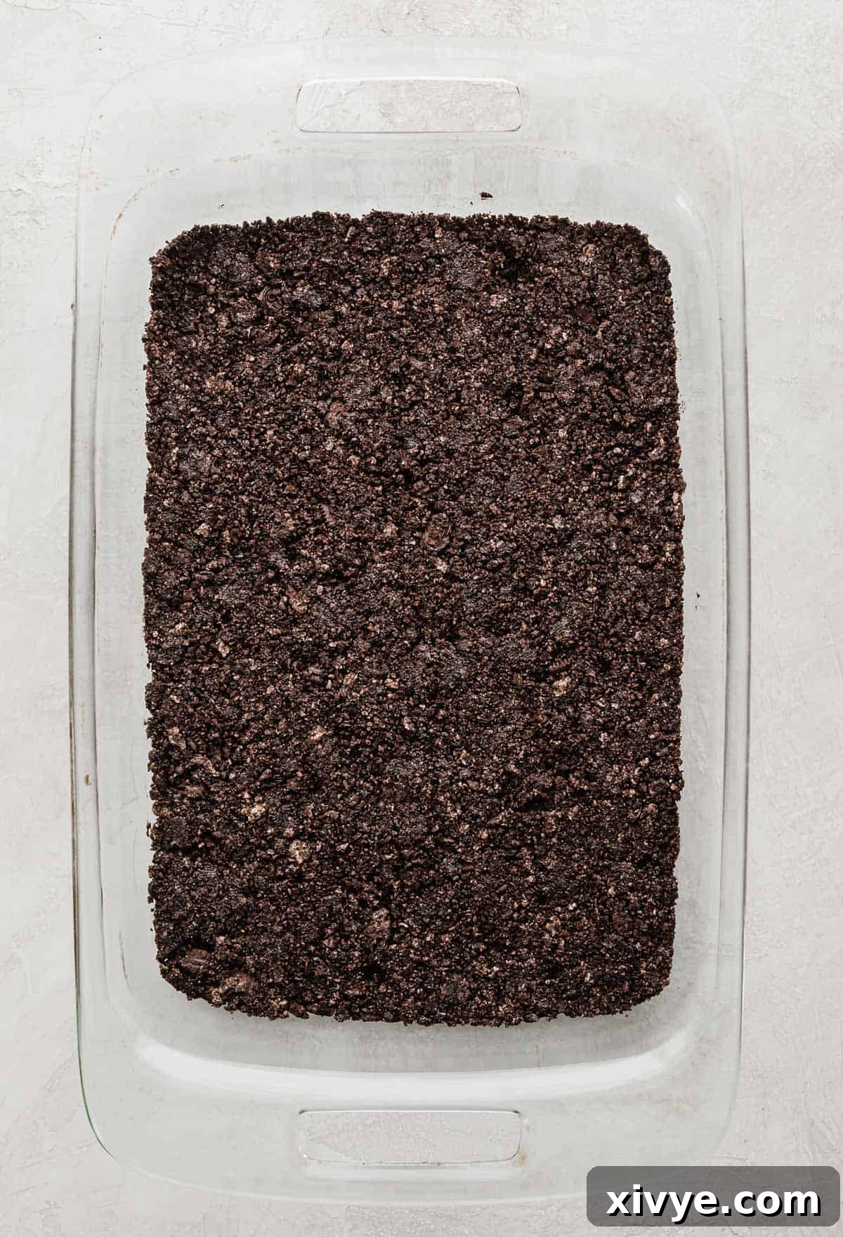 Dreamy Oreo Ice Cream Cake 4 Crushed oreo crust covering the bottom of a rectangular baking dish, forming the base of the ice cream cake.