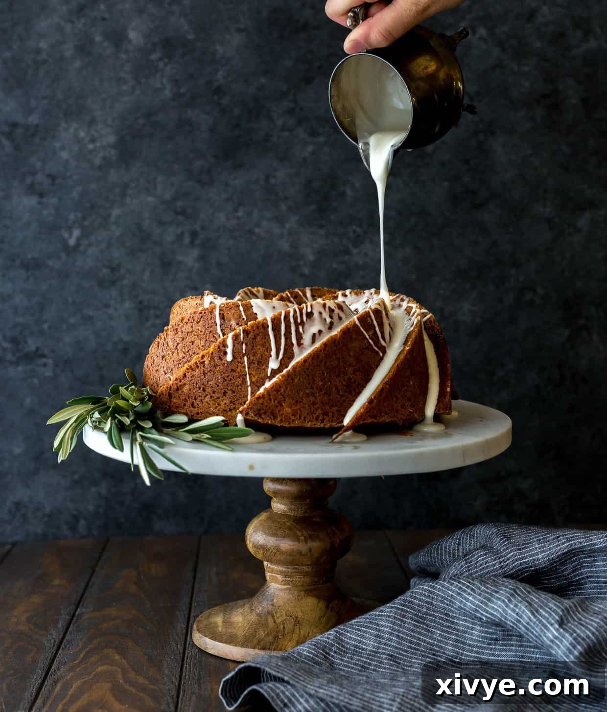 A beautiful gingerbread bundt cake on a cake stand, decorated with olive branches at its base, perfect for holiday gatherings.