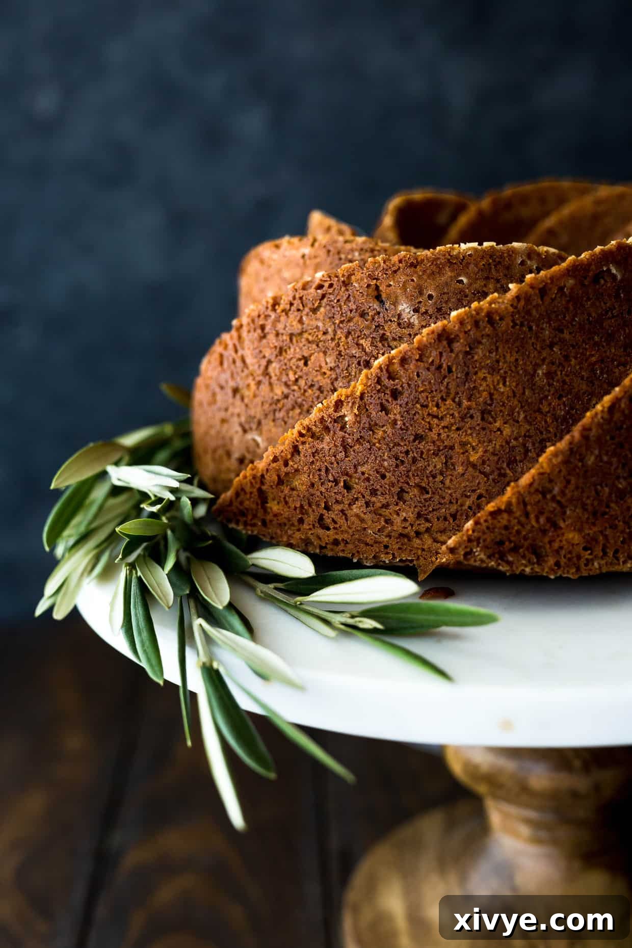Close up of a gingerbread bundt cake, made in a spiral cake pan, with olive branches at the base of the cake, showing its intricate design.
