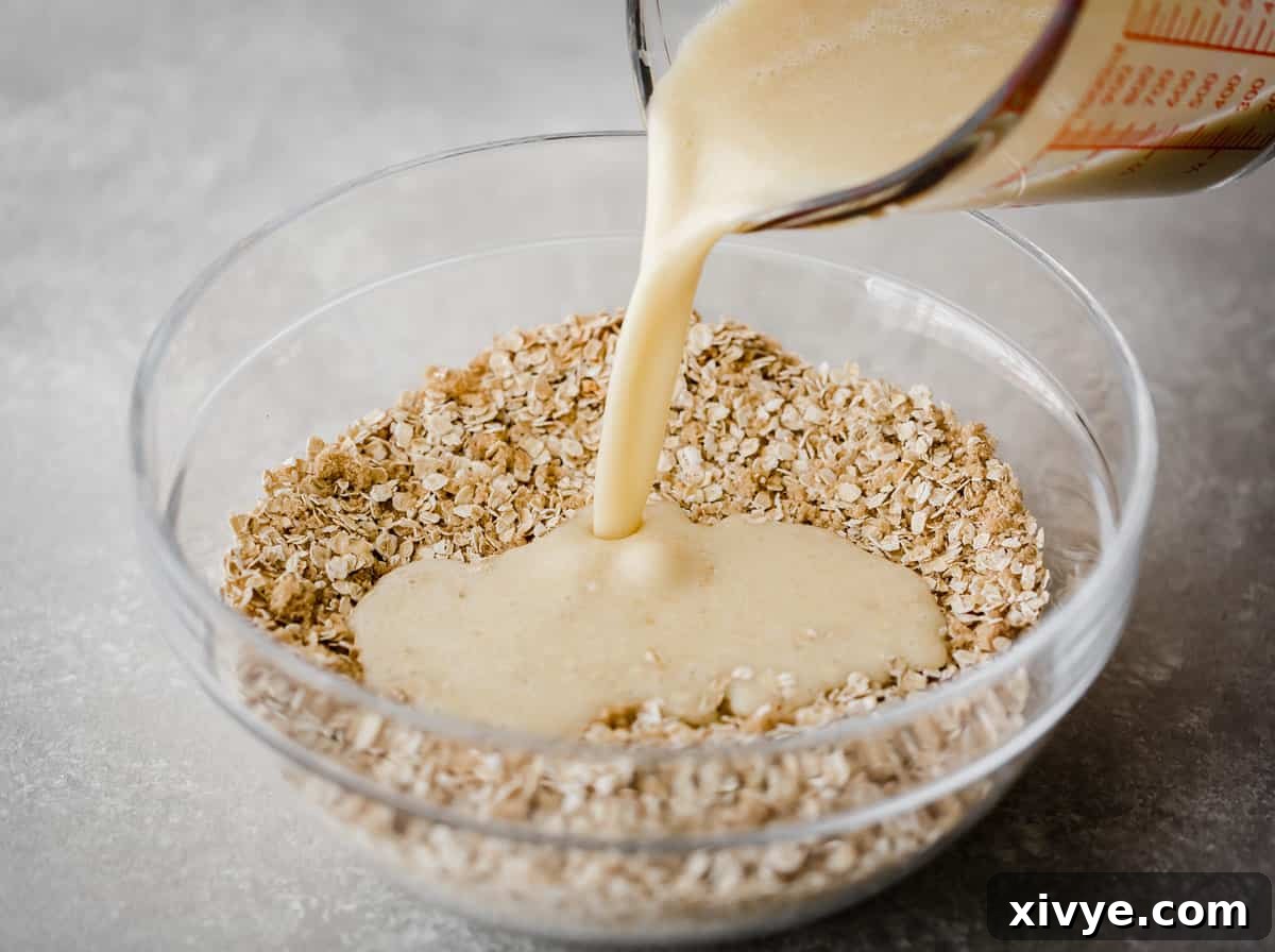 A light yellow colored liquid being poured into a glass bowl full of quick oats.