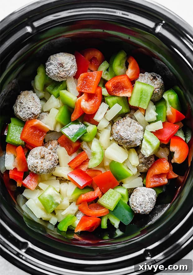 Delectable Sweet and Sour Slow Cooker Meatballs 6 A crock pot filled with frozen meatballs, red and green chopped bell peppers, and pineapple tidbits, showcasing all the main components before adding the sauce.