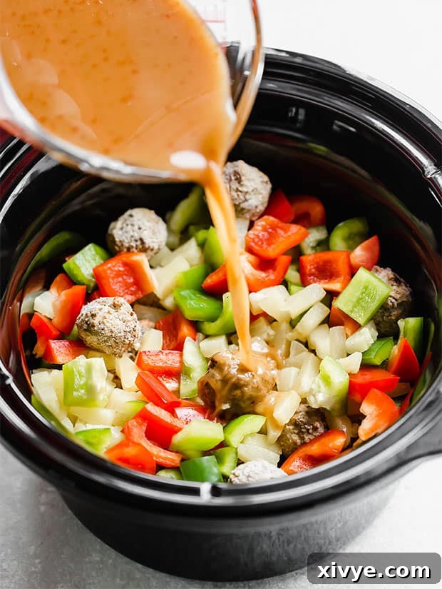 Delectable Sweet and Sour Slow Cooker Meatballs 7 The savory sweet and sour sauce being generously poured over the meatballs and other ingredients in a crock pot, preparing them for cooking.