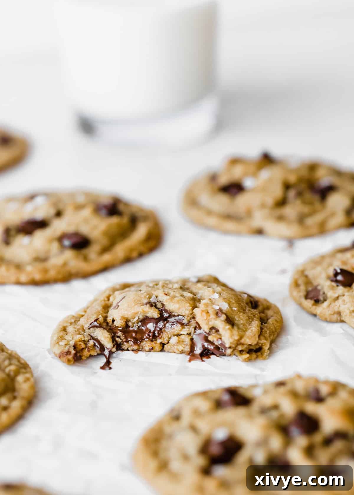Caramelized Butter Chocolate Chip Cookies 2 A perfectly baked Brown Butter Chocolate Chip Cookie with a bite taken out of it, resting on white parchment paper, showcasing its rich texture and melted chocolate.