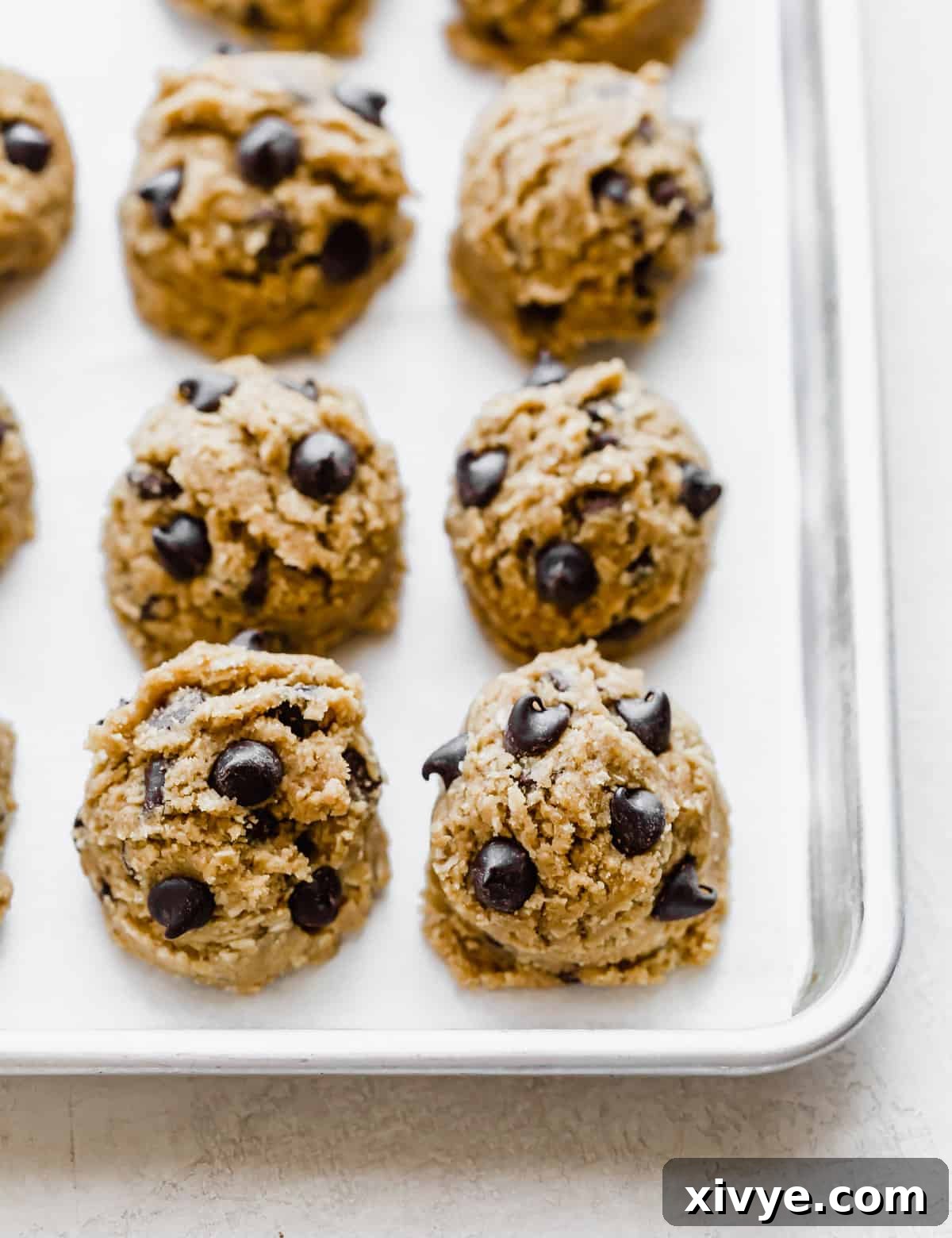 Caramelized Butter Chocolate Chip Cookies 9 Rows of perfectly scooped Brown Butter Chocolate Chip Cookie dough balls, generously topped with extra chocolate chips, arranged on a baking sheet, ready for the oven.
