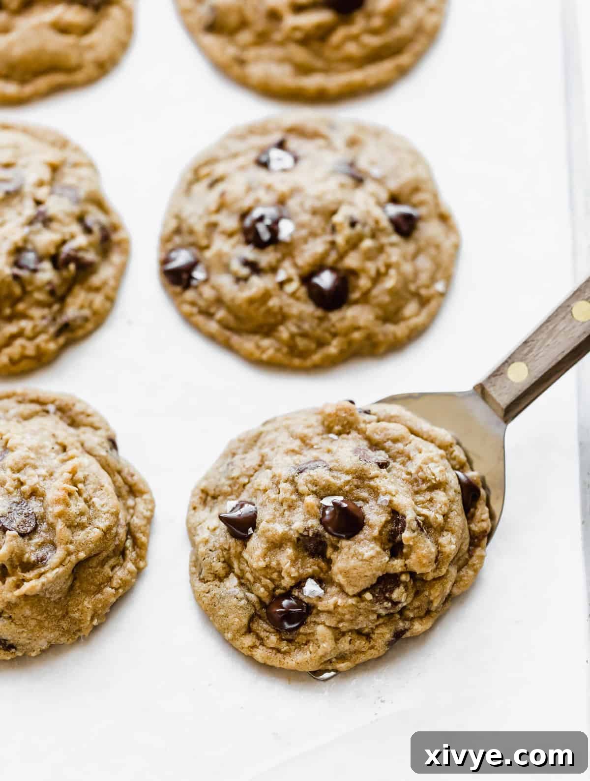Caramelized Butter Chocolate Chip Cookies 10 Freshly baked Brown Butter Chocolate Chip Cookies cooling on a white parchment paper-lined baking sheet, their golden edges and melted chocolate glistening.