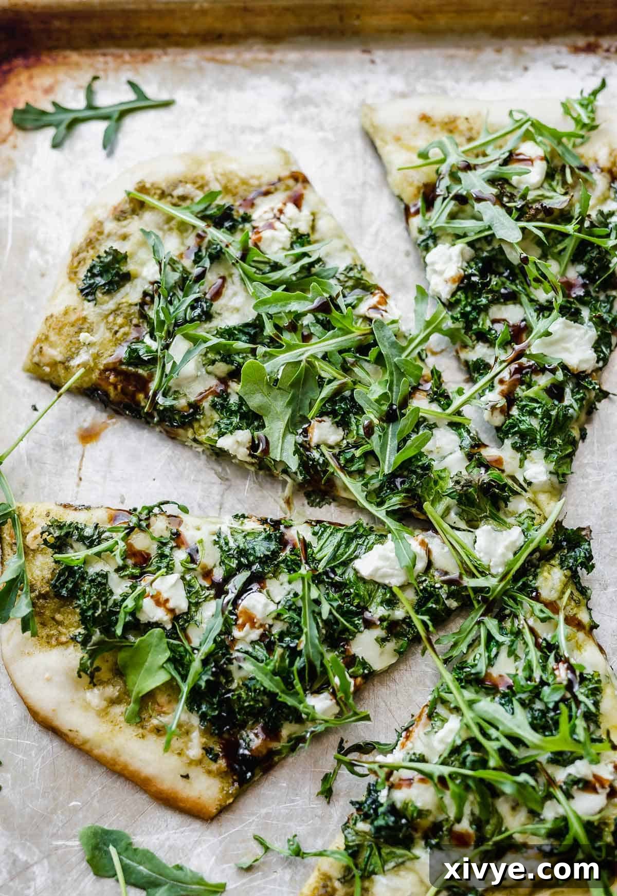 Close-up of kale pizza slices, garnished with fresh arugula and generous crumbles of goat cheese, ready to be served.