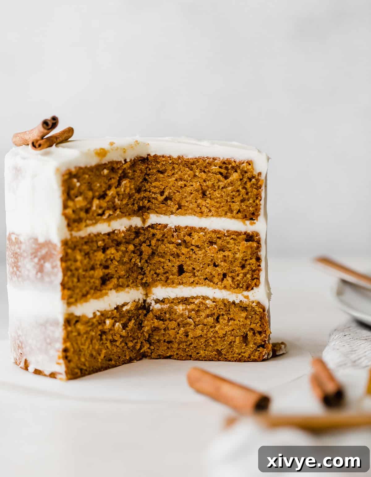 A beautifully frosted three-layer pumpkin cake on a clean white background, showcasing its rich orange hues and smooth cream cheese frosting between each layer.