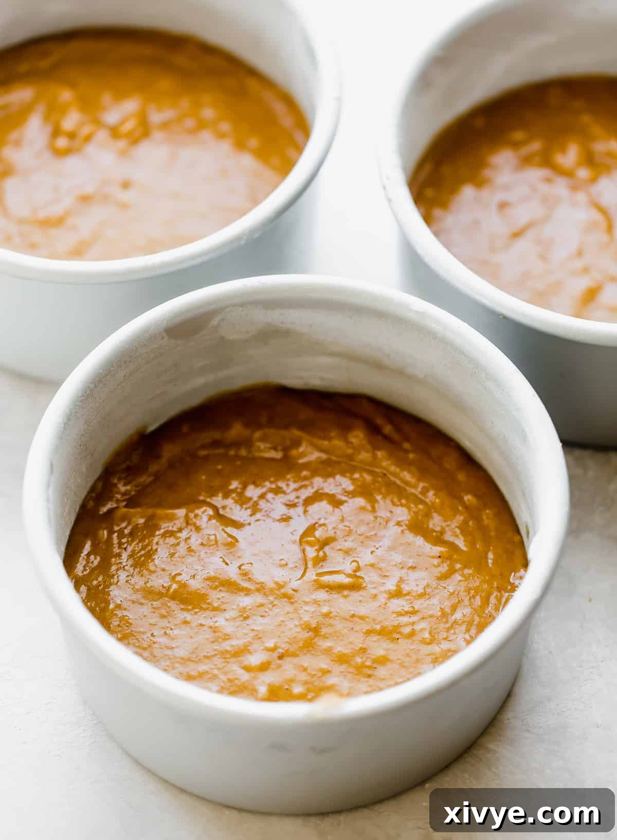 Three perfectly filled round cake pans, each containing an equal amount of raw pumpkin cake batter, neatly arranged and ready for baking.