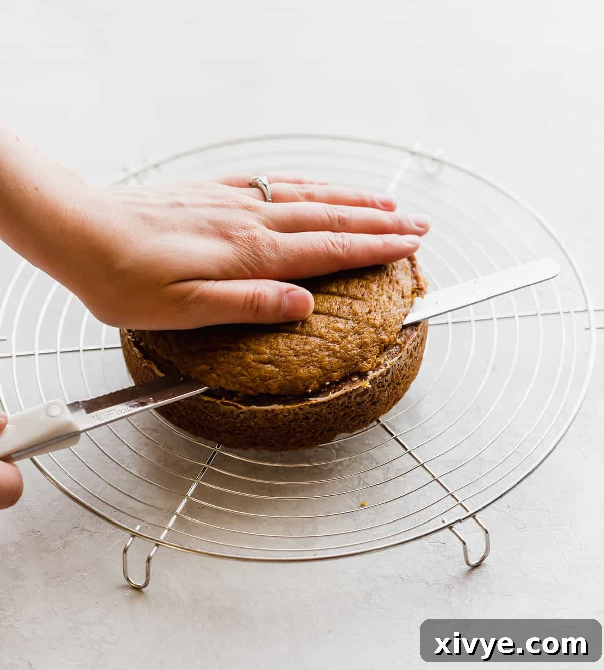 A baker expertly using a long serrated knife to level the top of a cooled pumpkin cake layer, ensuring a flat surface for perfect stacking.