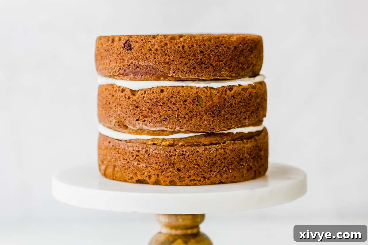 Three perfectly stacked pumpkin cake layers, generously frosted with cream cheese between each tier, displayed on an elegant cake stand.