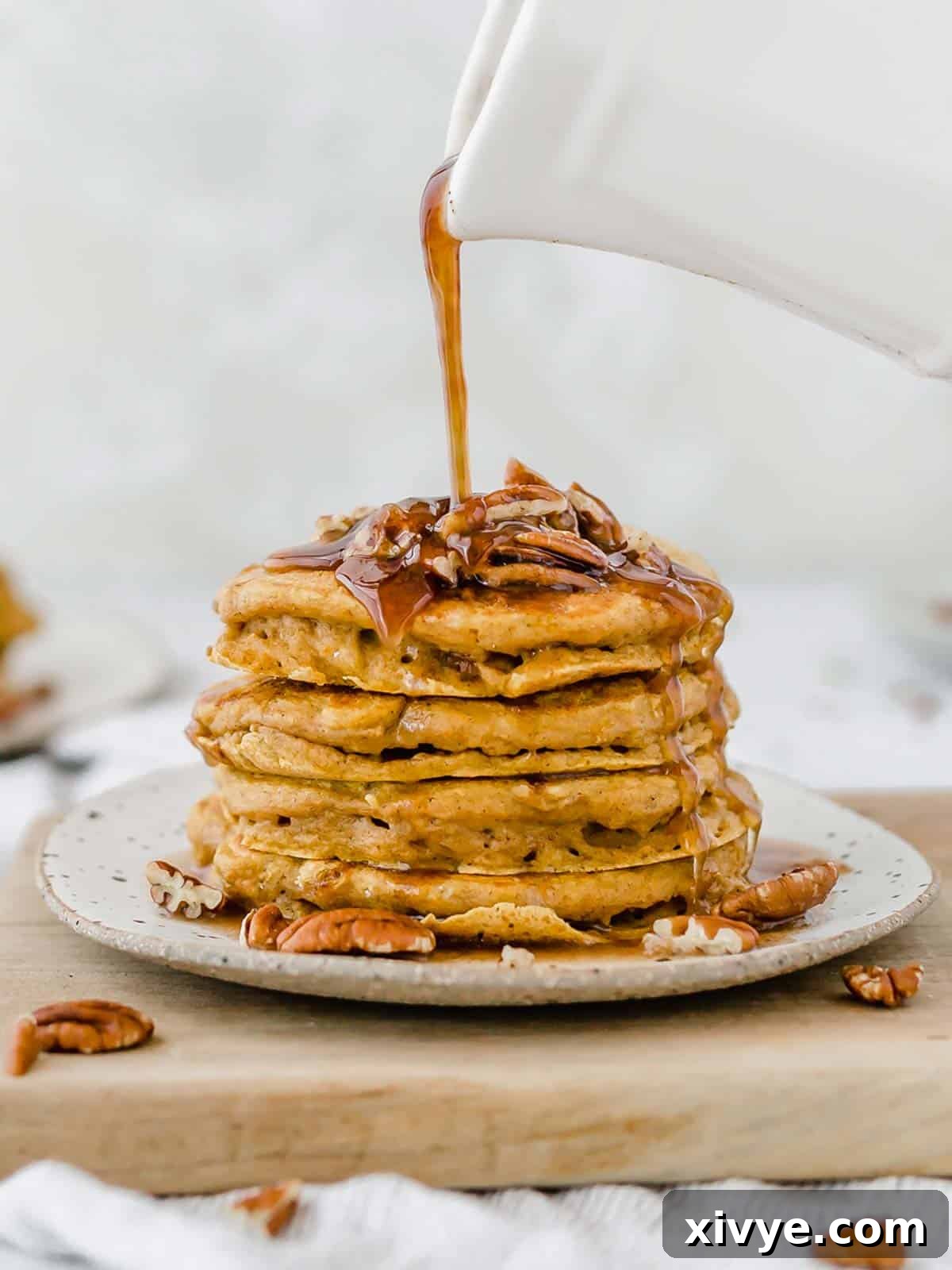 Spiced Pumpkin Pecan Pancakes 2 Pumpkin pancakes with pecans on top and syrup being poured over the pancake stack. The perfect fall breakfast.