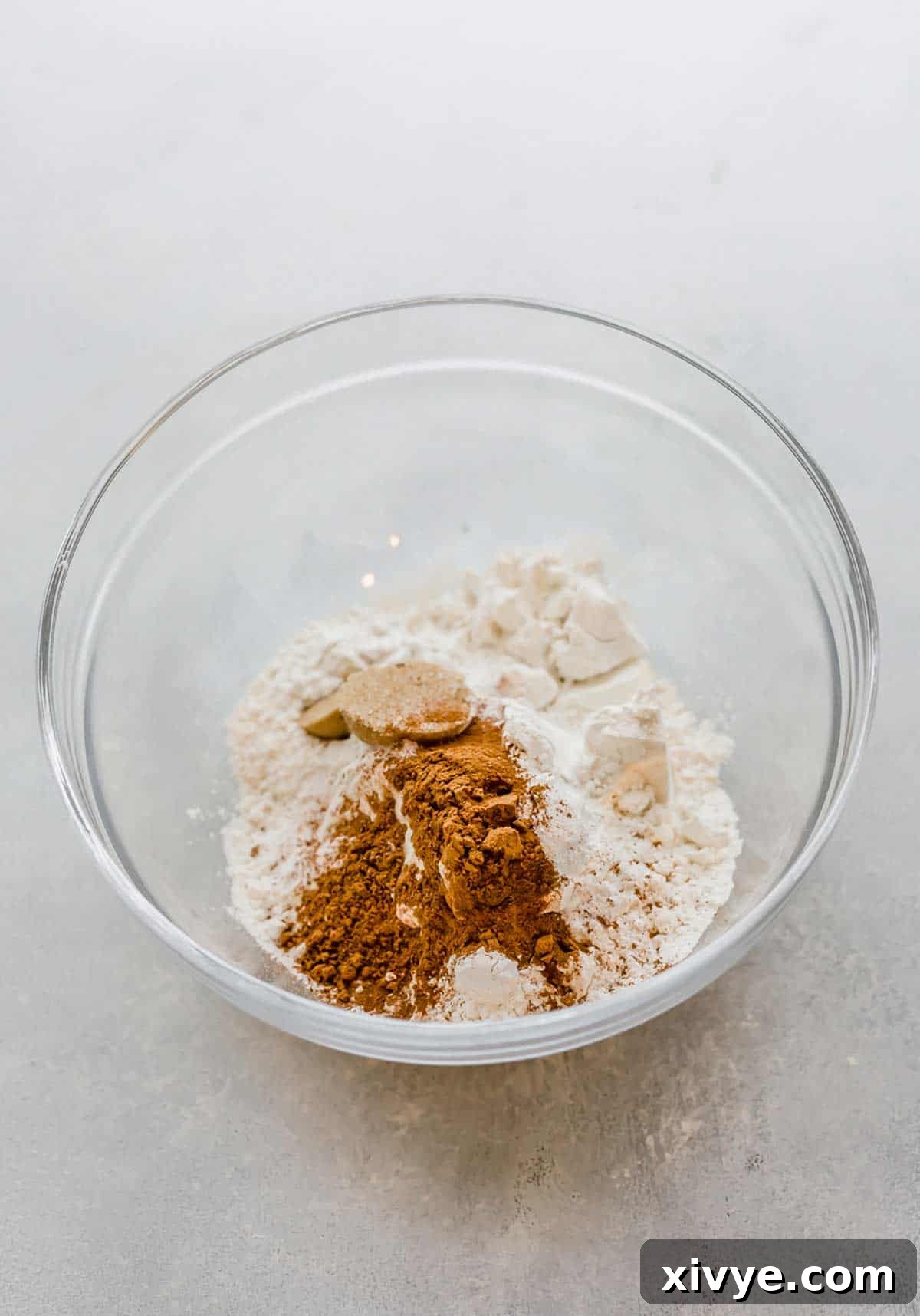 Spiced Pumpkin Pecan Pancakes 4 Dry ingredients used to make pumpkin pancakes, in a glass bowl on a light gray background.