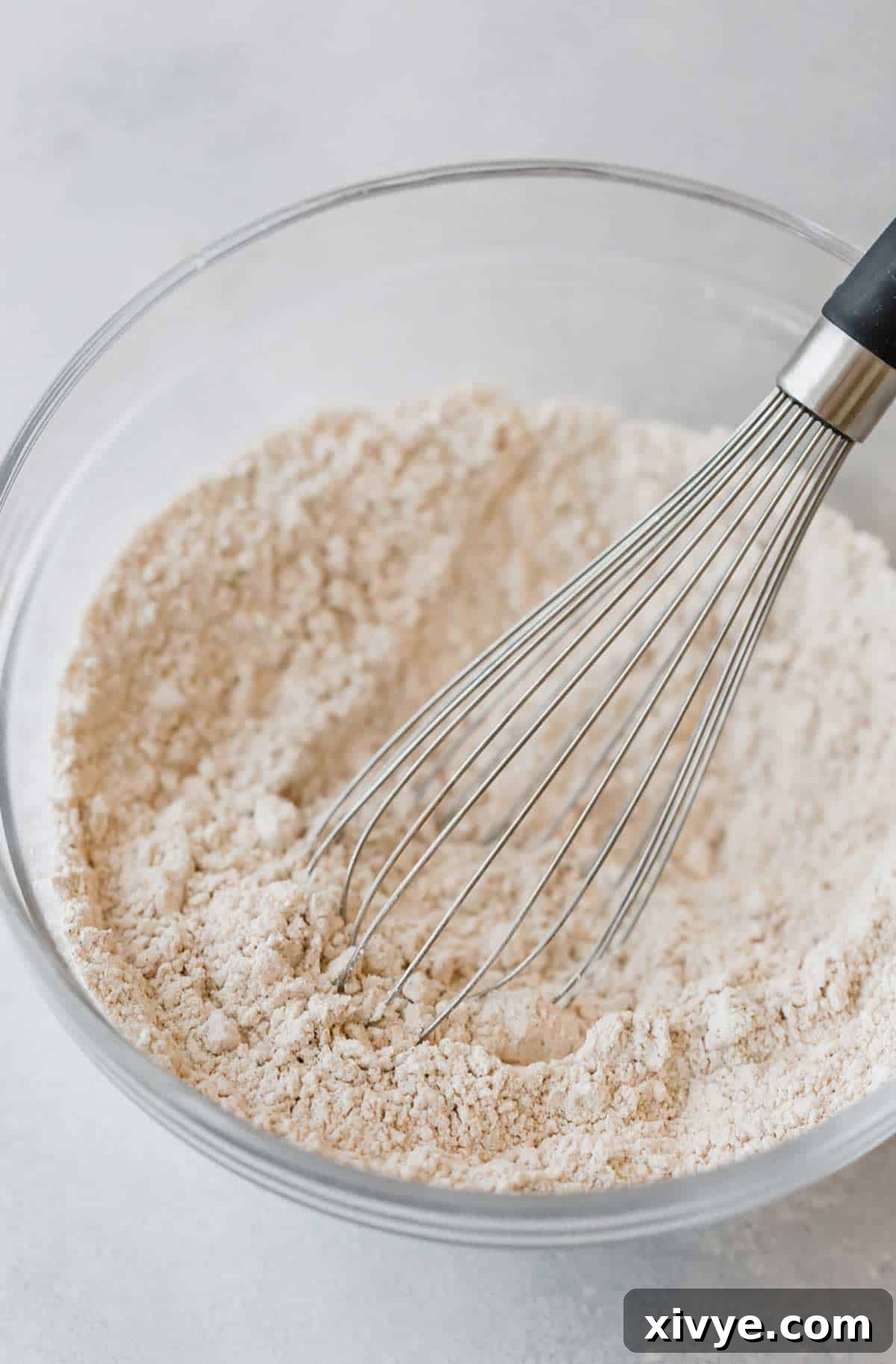 Spiced Pumpkin Pecan Pancakes 5 A whisk stirring the dry ingredients for making fluffy pumpkin pancakes, in a glass bowl.