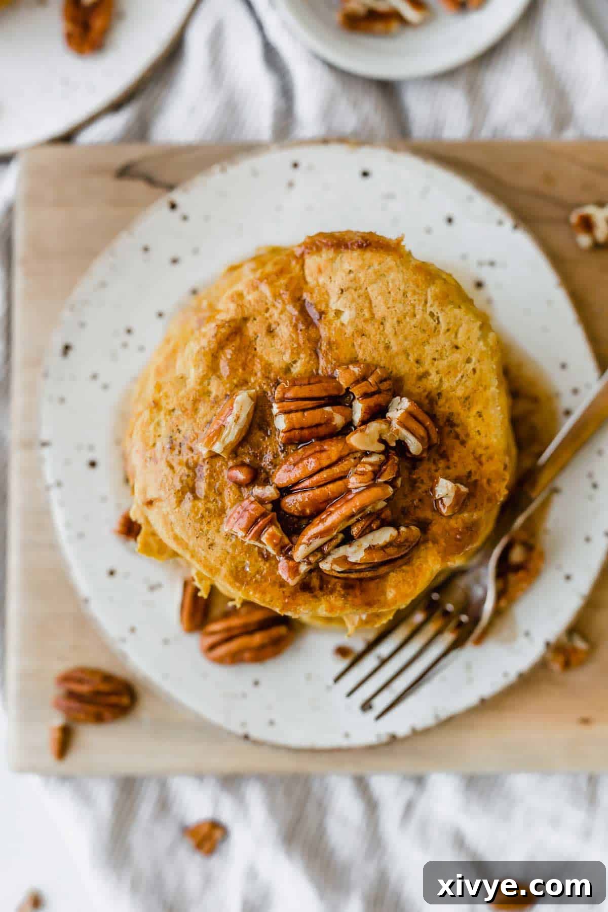 Spiced Pumpkin Pecan Pancakes 9 Overheard photo of fluffy pumpkin pancakes topped with chopped pecans, ready to be served.