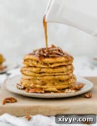 Spiced Pumpkin Pecan Pancakes 10 Fluffy pumpkin pancakes topped with pecans with syrup being poured overtop of the stack.