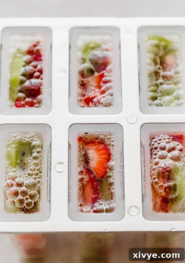 Popsicle mold filled with sliced kiwis and strawberries, showing the effervescent 7-Up being poured in, creating a bubbly effect.
