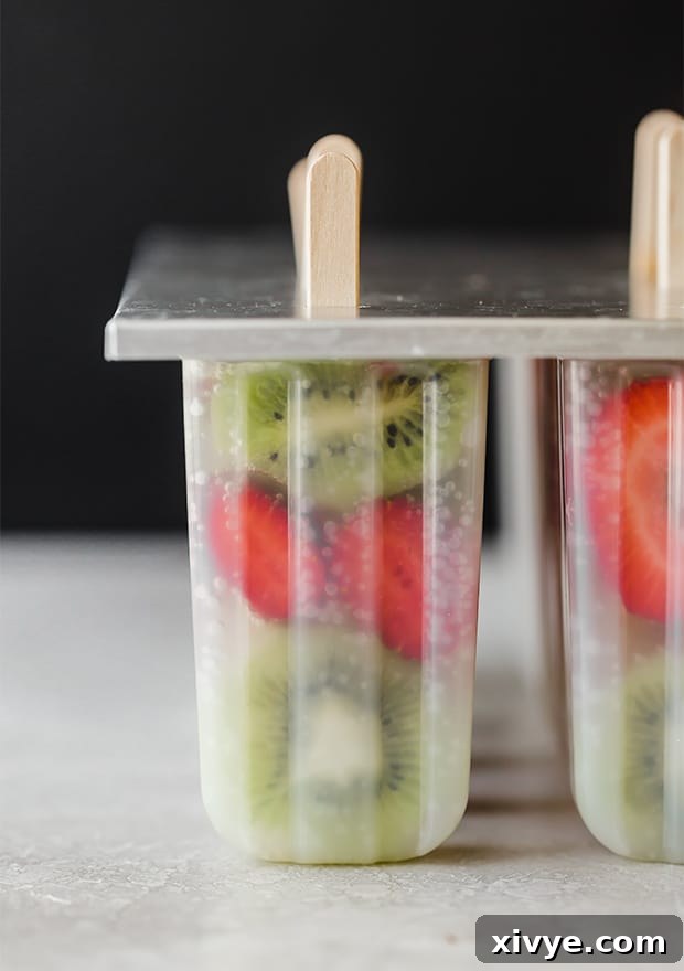 A full popsicle mold, completely frozen, with sliced kiwis, strawberries, and 7-up visible through the clear mold, and popsicle sticks inserted.