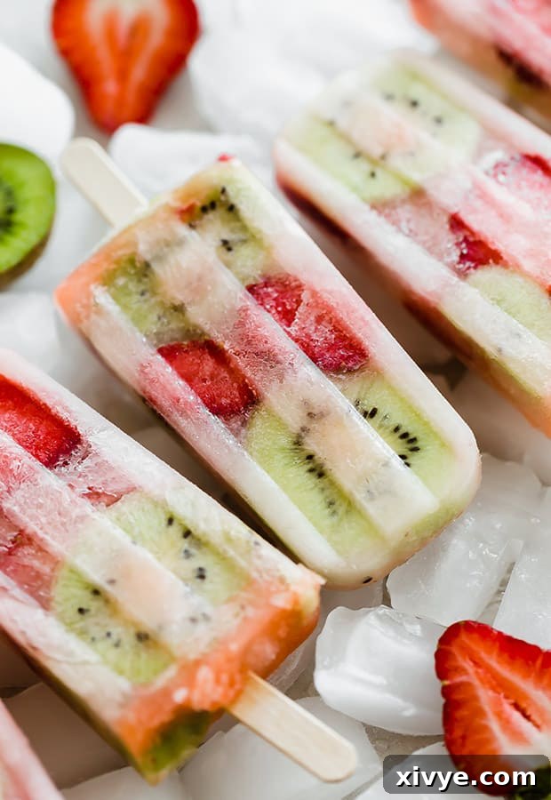Freshly removed kiwi strawberry popsicles arranged on a pile of frozen ice cubes, highlighting their refreshing appeal.