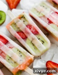 Kiwi strawberry popsicles sitting on a pile of frozen ice cubes.