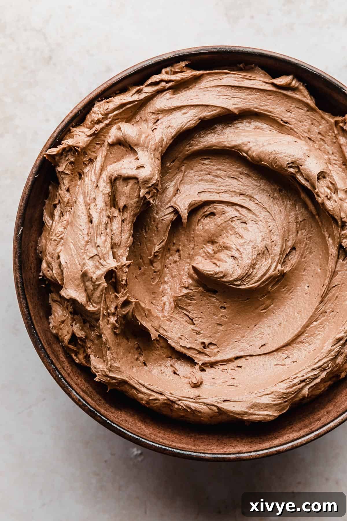 Decadent Chocolate Buttercream 2 A brown bowl full of light brown colored Chocolate Buttercream with Melted Chocolate, showcasing its smooth and creamy texture.