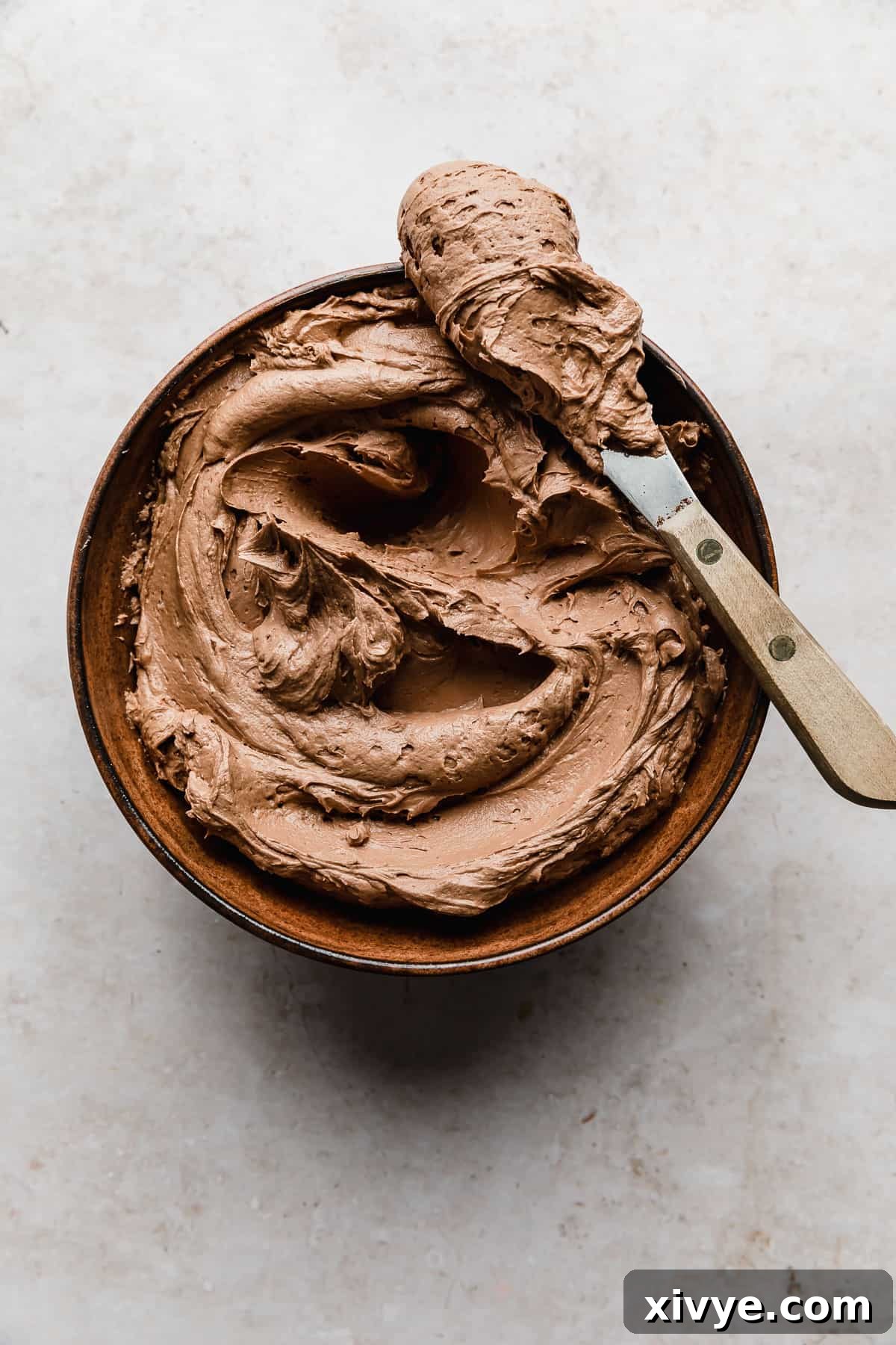 Decadent Chocolate Buttercream 14 A rich and creamy Chocolate Buttercream Frosting Recipe in a decorative brown bowl, set against a warm cream-textured background.