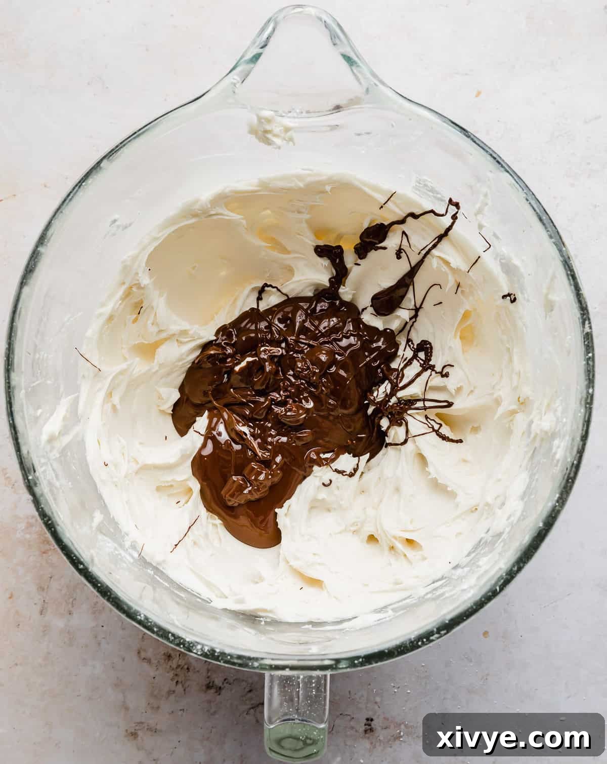 Decadent Chocolate Buttercream 8 Cooled melted chocolate gently poured over the creamed butter and powdered sugar mixture in a stand mixer bowl, ready to be combined into a rich chocolate frosting.