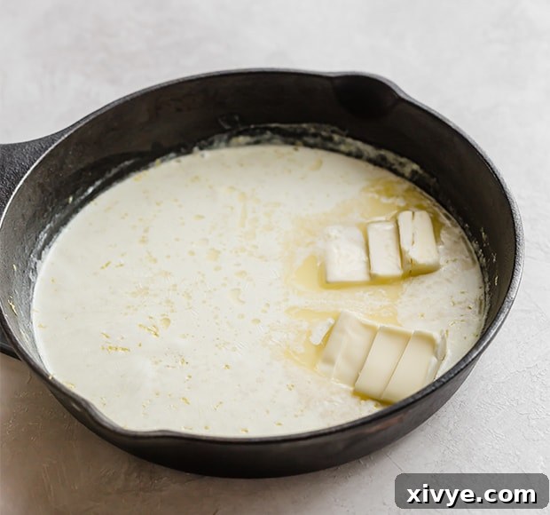 A skillet with heavy cream and butter slices in it.
