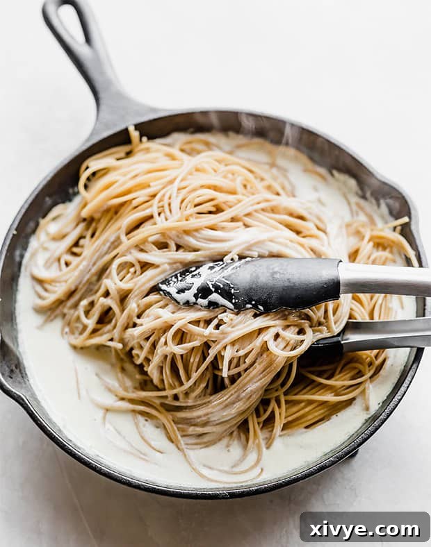 Kitchen tongs turning whole wheat pasta into lemon cream sauce.