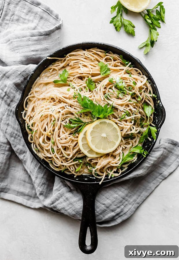 A black skillet full of lemon pasta noodles garnished with two lemon slices and fresh parsley.