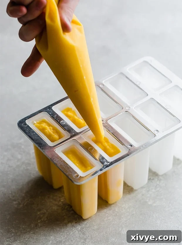 Sunshine Mango Pineapple Frosts 6 A pastry bag skillfully filling individual popsicle molds with the smooth, yellow-orange pineapple mango puree, demonstrating a clean filling technique.