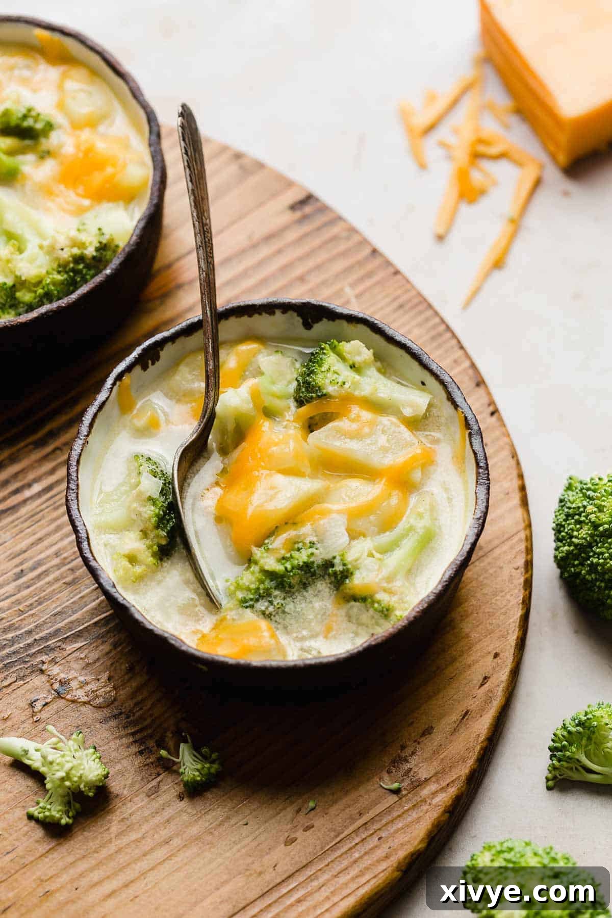 A steaming bowl of Cheesy Broccoli Potato Soup in a black-rimmed bowl, adorned with melted cheddar cheese and fresh parsley.