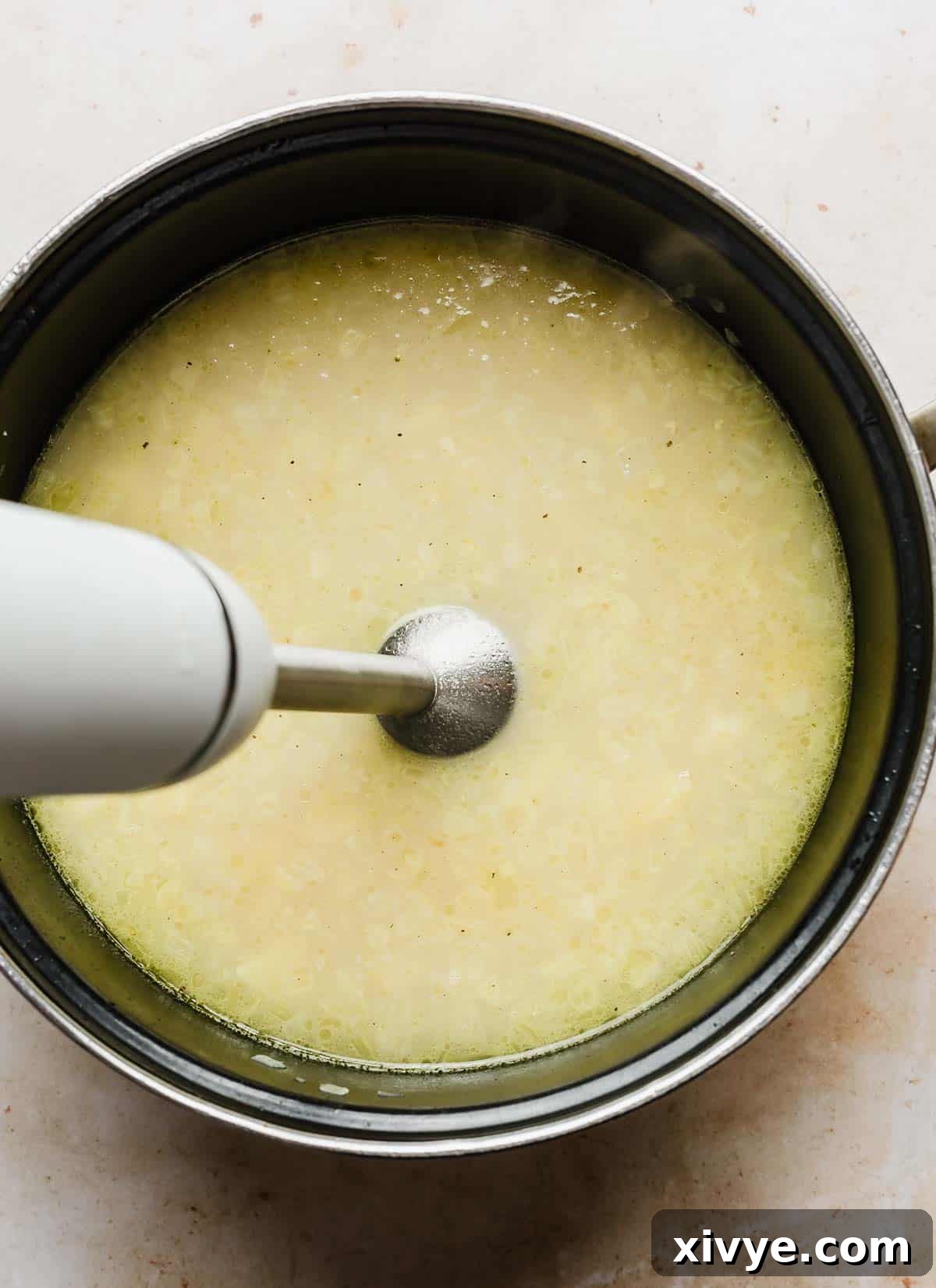 An immersion blender being used in a large pot to partially blend the potato and broth mixture for the soup.