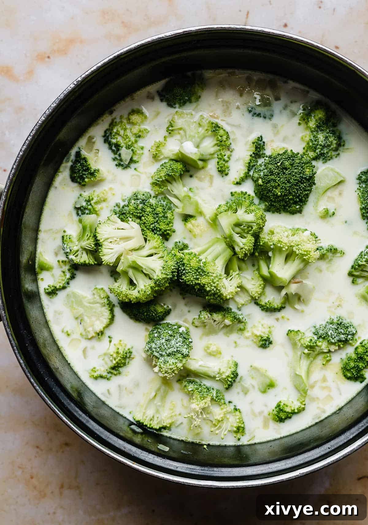 Vibrant green broccoli florets simmering in a large black pot with the creamy potato base, ready for cheese.