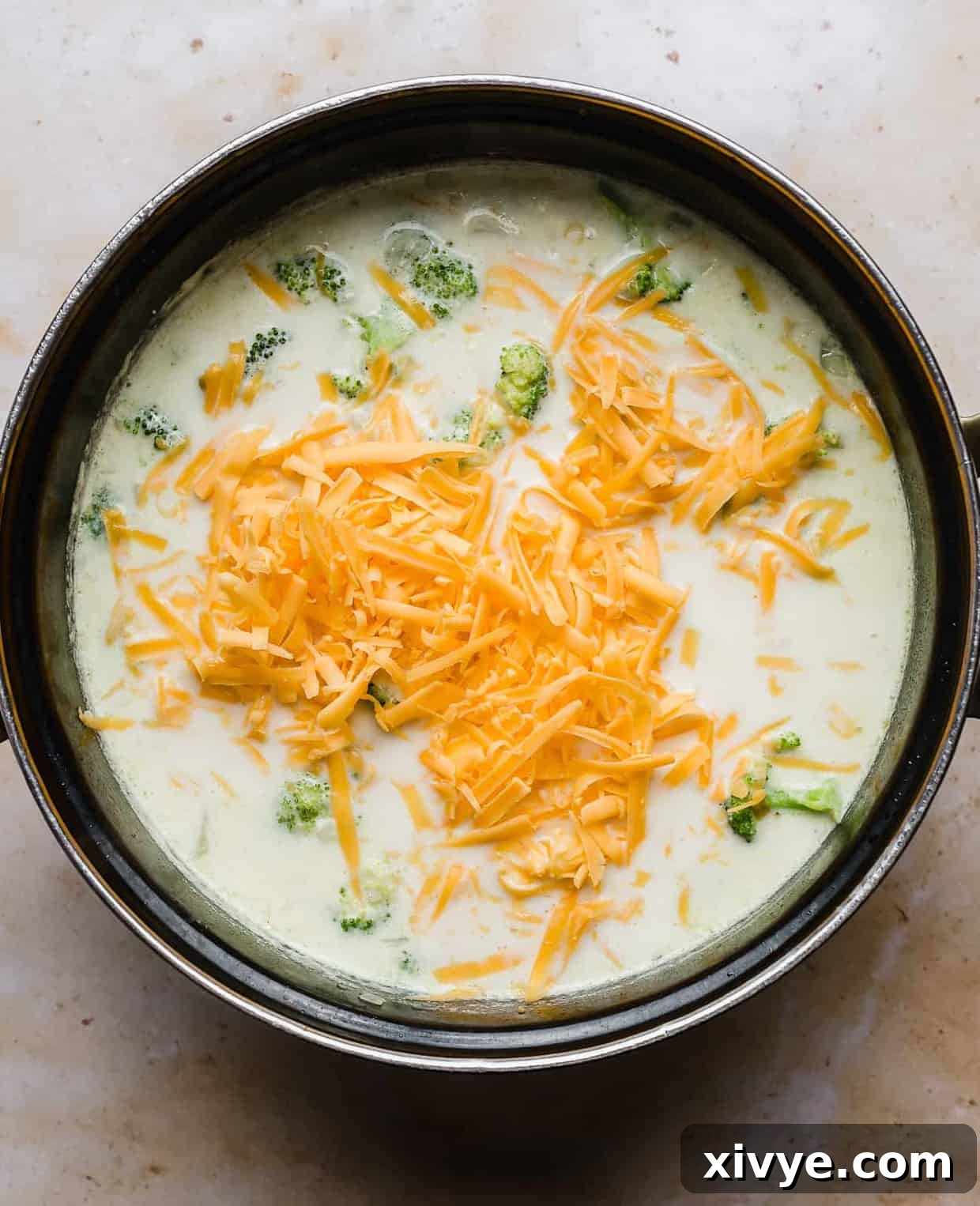 A large pot of rich Cheesy Broccoli Potato Soup, with a generous layer of shredded cheddar cheese melting on top, indicating its readiness to serve.