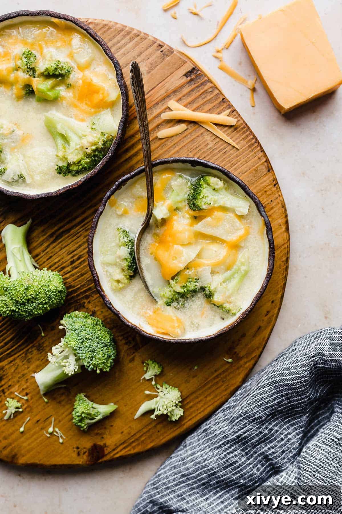 Overhead shot of two small black-rimmed bowls filled with Cheesy Broccoli Potato Soup, artfully arranged on a round wooden cutting board.