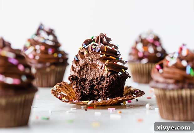 A decadent chocolate cupcake topped with a generous swirl of chocolate buttercream frosting and a colorful sprinkle mix. A bite has been taken, revealing its moist interior.