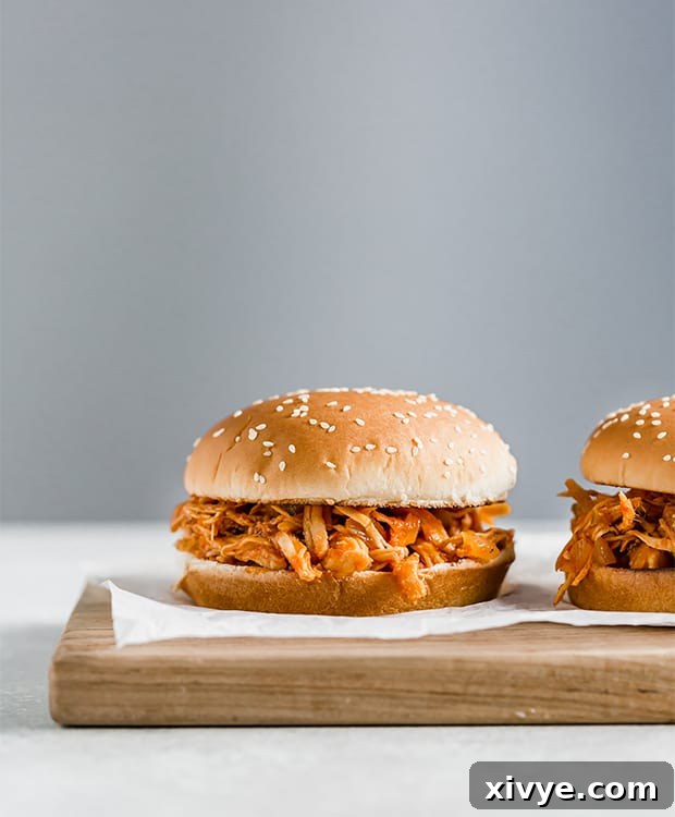 A perfectly assembled homemade BBQ chicken sandwich, resting on a rustic wooden cutting board, highlighting the juicy shredded chicken and vibrant sauce.