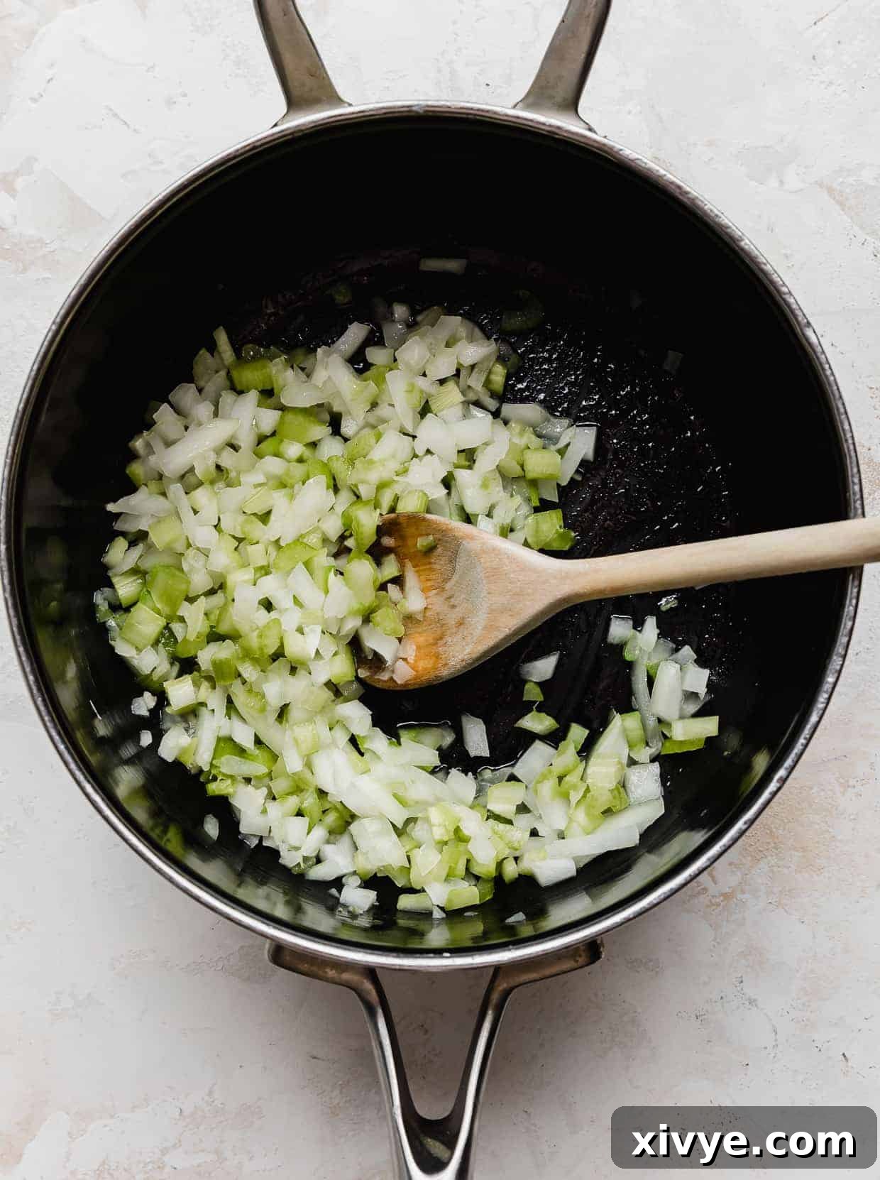 A saucepan on a stovetop, containing diced onion and celery gently sautéing in butter, preparing the base for the BBQ sauce.