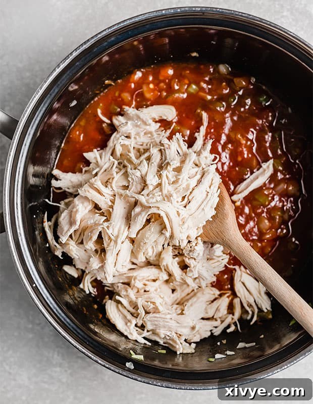 Shredded chicken being stirred into a thick, simmering BBQ sauce in a large pot, ensuring every piece is coated.