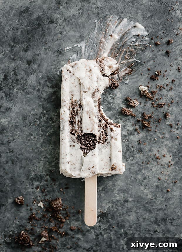 Decadent Cookies and Cream Pops 2 A delectable Cookies and Cream popsicle with a bite taken out of it, showcasing the crushed Oreo pieces.