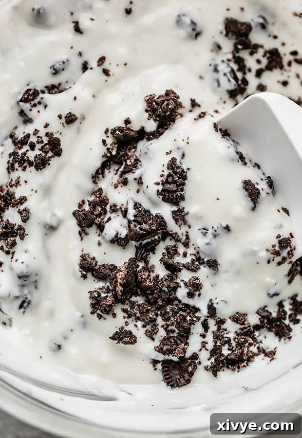 Decadent Cookies and Cream Pops 6 A close-up photo of crushed Oreo pieces being carefully mixed into the creamy Cookies and Cream popsicle base.