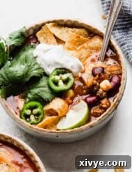 Taco Soup with sour cream, Fritos, cilantro, lime, and jalapeño for garnish.