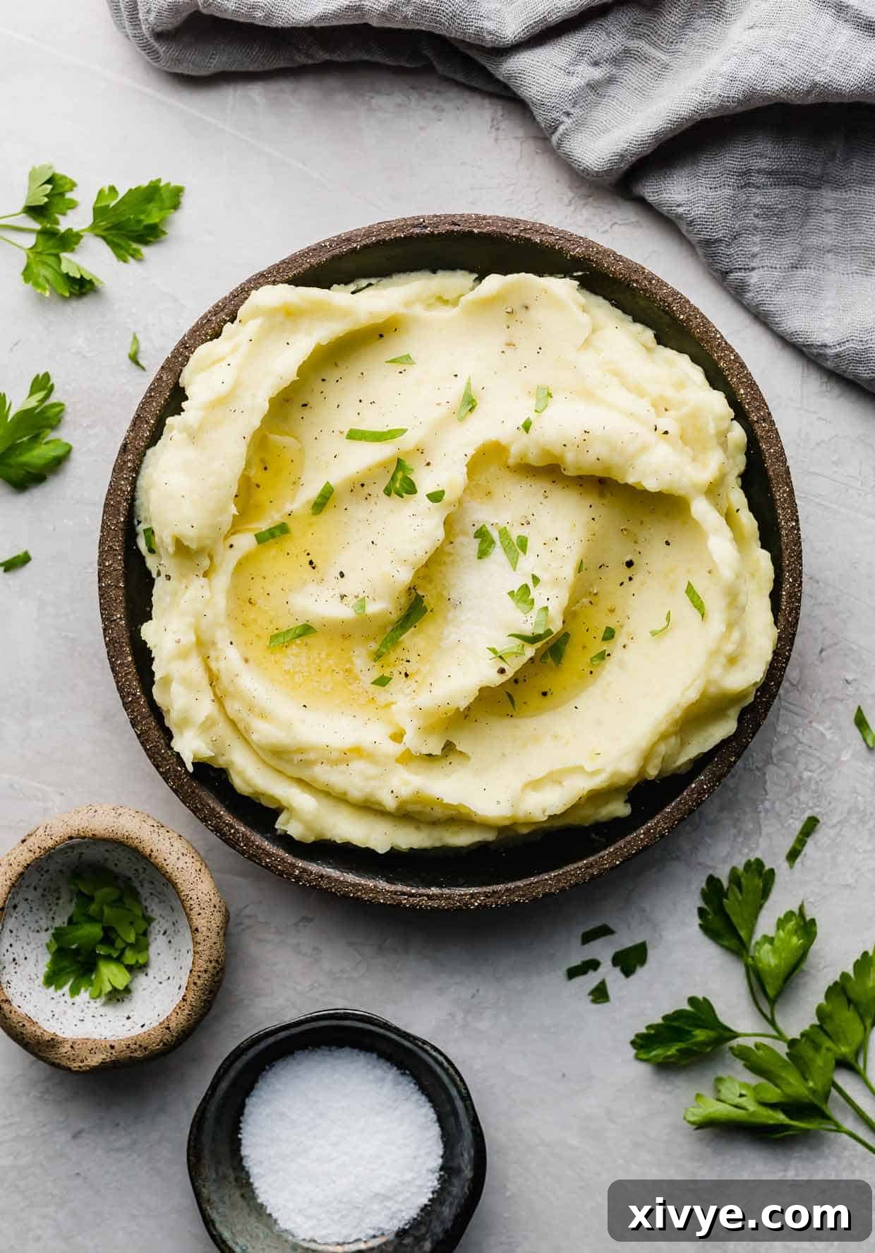 Swirled homemade mashed potatoes on a black plate topped with fresh chopped parsley for garnish.
