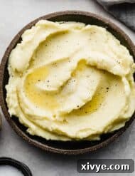 A black rimmed plate filled with Homemade Mashed Potatoes made with half and half and butter, garnished with fresh herbs.