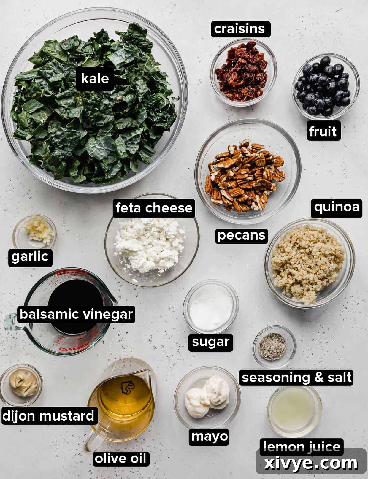 Kale and Quinoa Salad ingredients portioned into glass bowls on a light gray background. 