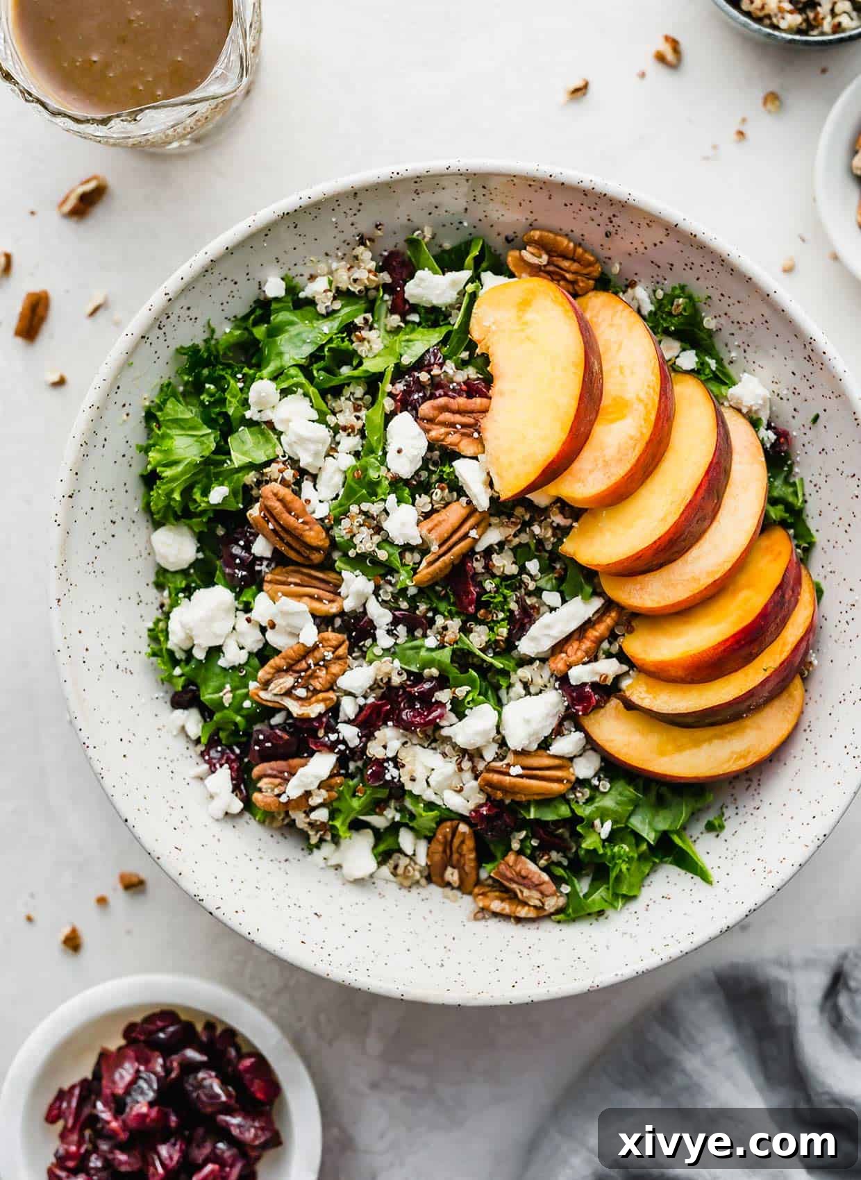 A Kale and Quinoa Salad with Cranberries and Feta and sliced peaches in a white bowl.