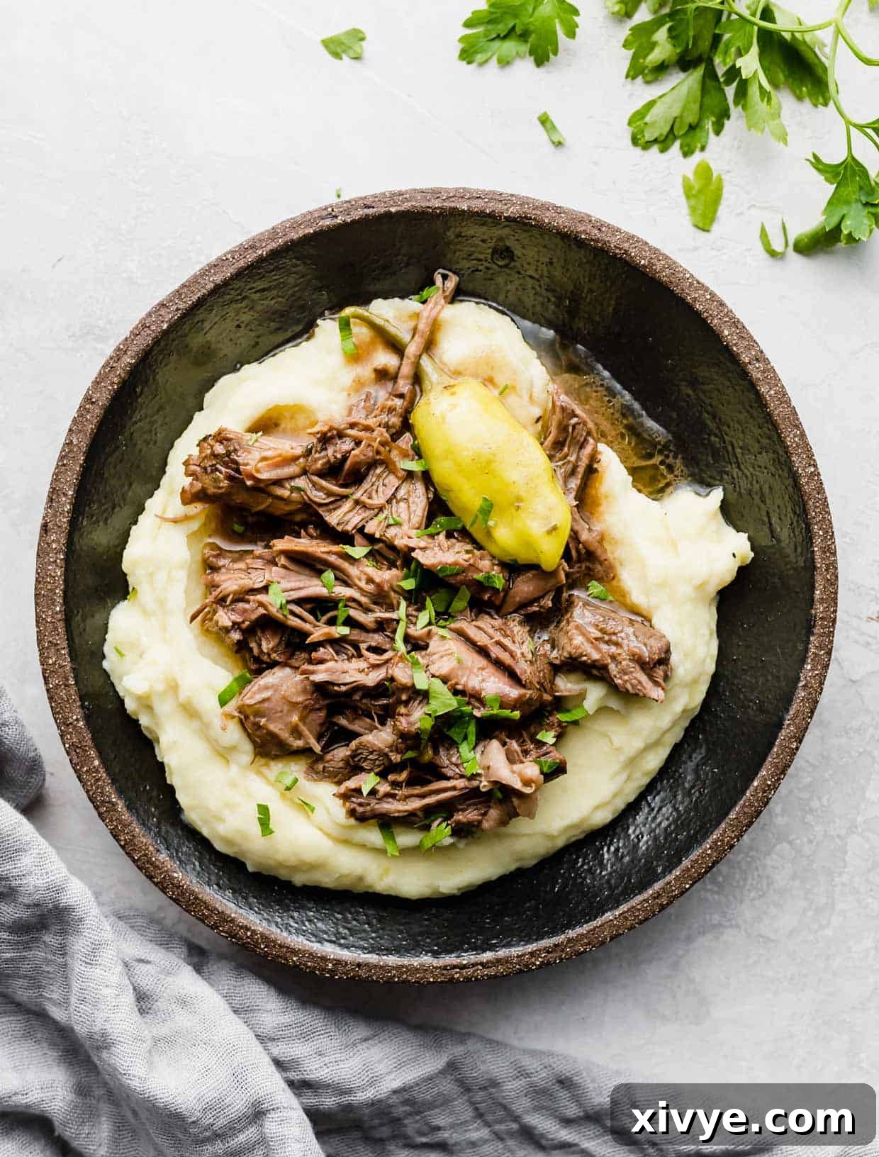 A serving of easy Mississippi Pot Roast made in a slow cooker, shredded and piled on top of a generous portion of creamy mashed potatoes.