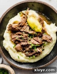 A black plate with creamy mashed potatoes and shredded Mississippi Pot Roast served on top.