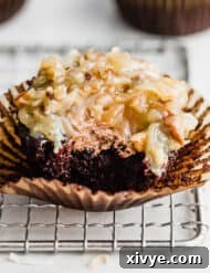 A bite taken out of a frosted German Chocolate Cupcake on a wire rack.